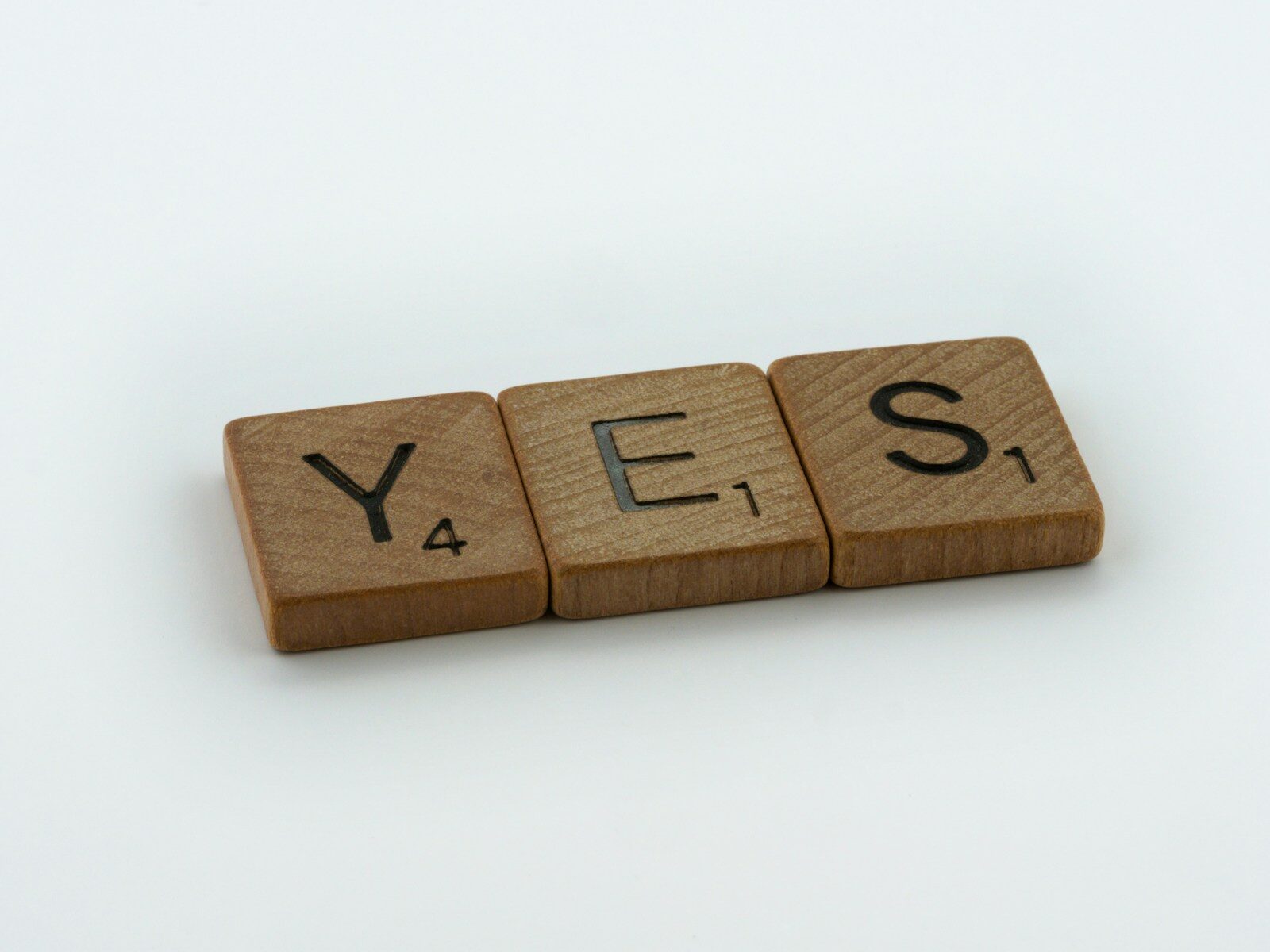 a wooden block spelling yes on a white background